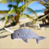 Felt narwhal ornament hanging on a palm tree branch.
