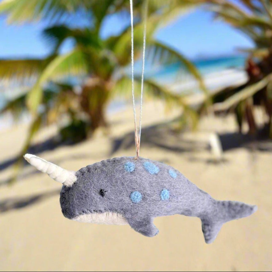 Felt narwhal ornament hanging on a palm tree branch.