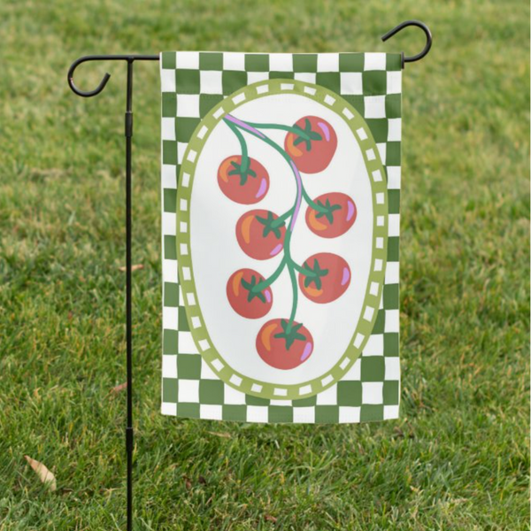Garden flag with tomato design on a green and white checkered background, attached to a pole in grass.