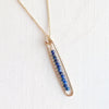 Gold necklace with a bar pendant featuring blue stones on a white background